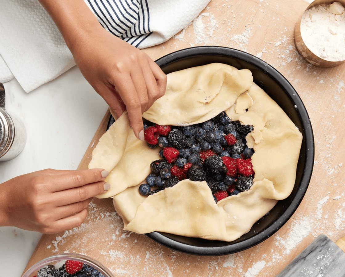 Image of a black, pure ceramic nontoxic pie plate which is free of metals and great for everyday use, from an Xtrema cookware review, a freeform pastry is being folded over fresh berries by a woman's hand.